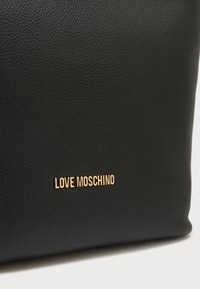 Μαύρη δερμάτινη τσάντα tote με υφή στην επιφάνεια και χρυσό λογότυπο «LOVE MOSCHINO» στο μπροστινό μέρος. Ορθογώνιο σχήμα.