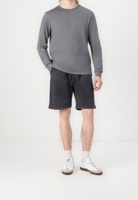 Graues Langarmshirt kombiniert mit dunklen Denim-Shorts. Das Outfit wird von weißen Sneakers mit grauen Akzenten und hellen Socken ergänzt.