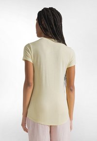 Jasnożółta dopasowana koszulka z krótkimi rękawami, okrągłym dekoltem i zaokrąglonym dołem. Gładka tekstura, miękki materiał oraz minimalne detale szwów.