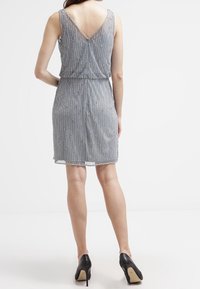 Gaun tanpa lengan berwarna perak abu-abu dengan desain manik-manik, punggung berbentuk V, pinggang yang diikat, dan panjang hem setinggi lutut. Dipasangkan dengan sepatu hak tinggi berwarna hitam.