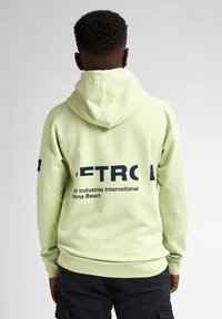 Felpa verde chiaro con cappuccio e tasca a marsupio, con grande testo nero sul retro e tessuto a coste ai polsini e all'orlo.