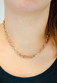 Kraftig rosaguld kæde med ovale led, glat overflade, båret om halsen. Synlig udskæring af en mørk top.