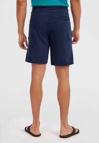 Shorts bleu marine en tissu doux, avec une poche arrière et une coupe décontractée, se terminant juste au-dessus du genou, assortis à des tongs noires.