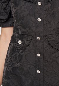Tissu jacquard floral noir avec boutons brillants en strass et deux poches devant sur une robe ou un chemisier.