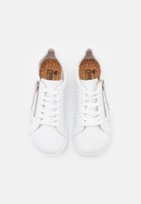 Baskets blanches en cuir avec des détails perforés, lacets plats blancs et une fermeture éclair sur le côté. Semelle intérieure en liège pour un confort supplémentaire.