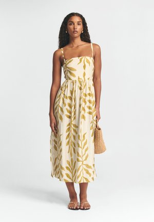 Biele maxi šaty s potlačou žltých listov, štíhle ramienka, zúžený pás a splývavá sukňa. Doplnkové šaty sú s tkanou taškou.
