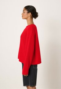 Pull en tricot rouge à côtes avec une coupe décontractée, col rond et manches longues, associé à une jupe en denim noir.