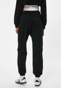 Sorte træningsbukser med elastisk talje og manchetter, der har en løs pasform og sidelommer. Sammen med hvide sneakers med sorte detaljer.