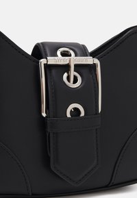 Sangle en cuir noir avec boucle argentée gravée "Steve Madden" sur un sac ou accessoire structuré noir.