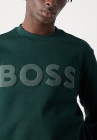 Felpa verde con scollo rotondo a costine e logo "BOSS" imprimato in un verde più scuro. Tessuto di trama liscia.
