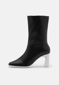 Botín negro de piel con punta afilada y tacón bloque blanco. Textura suave y diseño minimalista, adecuado para diversas ocasiones.