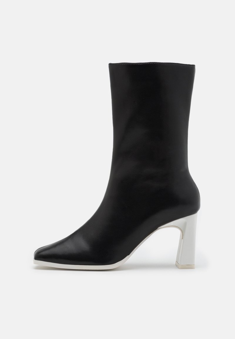 Botín negro de piel con punta afilada y tacón bloque blanco. Textura suave y diseño minimalista, adecuado para diversas ocasiones.