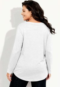 Biała koszula z długim rękawem, zaokrąglonym dołem i luźnym krojem. Tkanina wydaje się miękka i gładka, z delikatnym połyskiem.