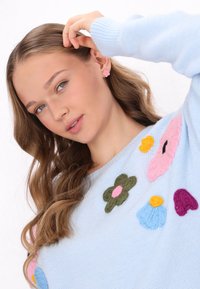 Maglione lavorato a maglia blu chiaro con applicazioni floreali colorate in rosa, giallo, blu e verde; tessuto morbido e scollatura rotonda.