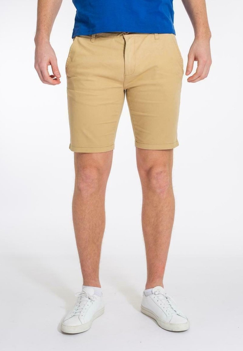 Shorts kaki en coton, avec un devant plat, des poches latérales et un ourlet retroussé, associés à des baskets blanches et un t-shirt bleu.