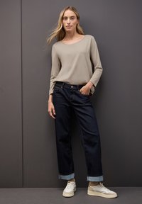Beige Langarmshirt, dunkelblaue weit geschnittene Jeans mit umgeschlagenem Saum und weiße Sneakers mit grauen Akzenten. Glatter Stoff und lässige Passform.