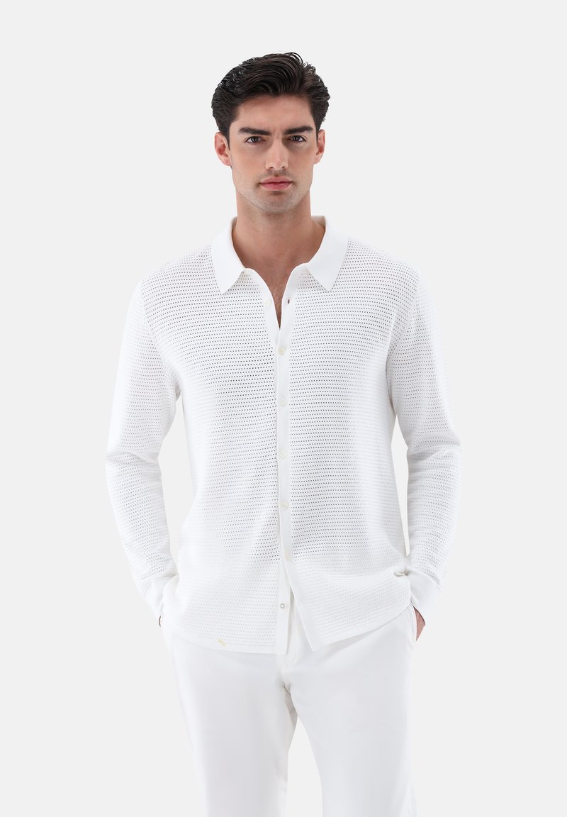 Weißes Langarmhemd aus strukturiertem Mesh-Gewebe, mit einem Button-Down-Kragen und Frontknöpfen, kombiniert mit weißen Hosen.