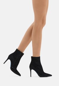 Stivali neri alla caviglia con un motivo a zigzag, alti tacchi a stiletto e una texture morbida. Punta affusolata e dettaglio di design simile a una calza.