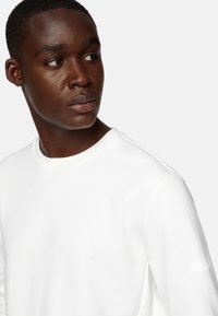 Felpa bianca con colletto rotondo, caratterizzata da una texture morbida, con un sottile logo sulla manica sinistra e una vestibilità comoda.