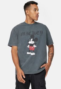 Pohledný bavlněný tričko v antracitově šedé barvě s grafikou Mickey Mouse v červených šortkách. Krátké rukávy, kulatý výstřih, volný střih a minimální detaily.