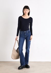 Navy long-sleeve top paired with blue flared jeans. Model carries a beige bag and wears black platform boots. Simple, clean design, no patterns.