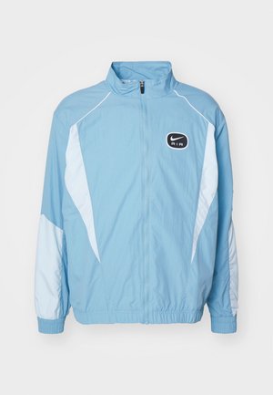 Vaaleansininen Nike Air -treenitakki, jossa on valkoiset paneelit, täyspitkä vetoketju, korkea kaulus sekä joustavat hihansuut ja helma.