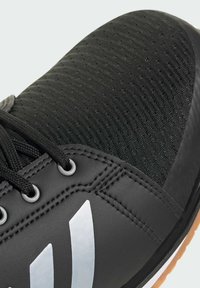 Black athletic shoe featuring a textured upper, smooth synthetic accents, gray eyelets, and white logo. Flat laces and a rubber sole.