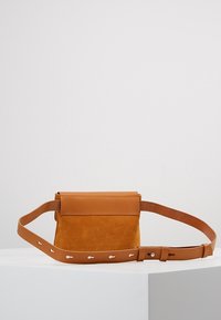 Borsa a tracolla in suede e pelle marrone con una forma rettangolare semplice, dotata di patta pieghevole e tracolla regolabile con piccoli dettagli.