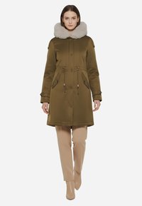 Parka verde oliva con grande colletto in pelliccia grigia chiara, vita con cordoncino, due tasche anteriori e polsini con bottoni. Texture liscia.