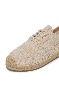 Espadrille beige con intrincado bordado floral, punta redondeada, parte superior texturizada y suela envuelta en yute. Presenta ojales y cordones en tono dorado.