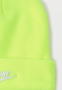 Neon zelena pletena kapa s rebrastom teksturom i presavinutim rubom. Ima bijeli izvezeni logo "NIKE" sa detaljem swoosh.