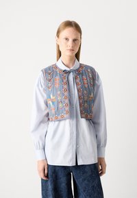 Camicia azzurra chiara con un gilet ricamato grigio che presenta motivi floreali e geometrici in colori vivaci, maniche lunghe e un papillon.