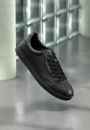 Schwarzer Ledersneaker mit strukturierter Oberfläche, flachen Schnürsenkeln, abgerundeter Zehe und Gummisohle. Verfügt über ein Logodetail an der Seite.