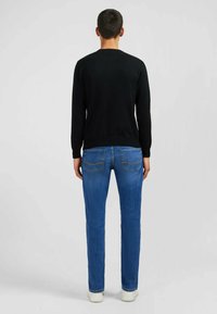 Pull en tricot noir à manches longues associé à un jean droit bleu clair. Il présente une couture simple et des baskets blanches.