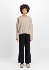 Sudadera oversized beige con hombros caídos, puños y dobladillo acanalados; combinada con pantalones de pierna ancha negros y zapatos grises. Diseño simple.