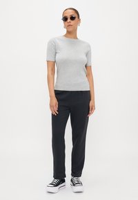 Top grigio a maniche corte, pantaloni neri e sneakers platform nere. Accessori includono occhiali da sole rotondi e orecchini a cerchio. Design semplice e aderente.