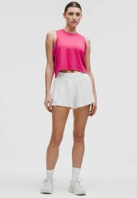 Rosa ärmelloses Oberteil und weiße Sportshorts. Das Oberteil hat ein kurzes Design; die Shorts zeichnen sich durch einen lockeren Schnitt und einen elastischen Bund aus. Weiße Sneaker.