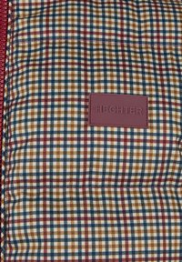 Braun, marineblau und weiß kariertes Gewebe mit einer strukturierten Oberfläche; versehen mit einem bordeauxroten Lederetikett, das mit "HECHTER" geprägt ist.