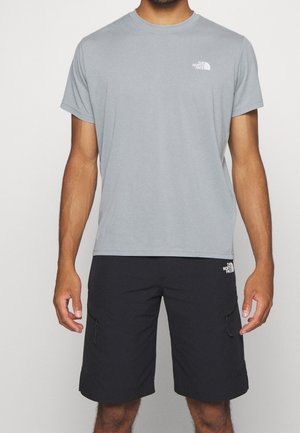 Mężczyzna ubrany w jasnoszarą koszulkę z krótkim rękawem i okrągłym dekoltem oraz czarne krótkie spodenki do kolan z logo The North Face na piersi i udzie.