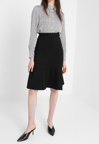 Svart figursydd kjol med utsvängd nederkant, parat med en svart och vit randig långärmad skjorta. Glansiga svarta spetsiga skor.