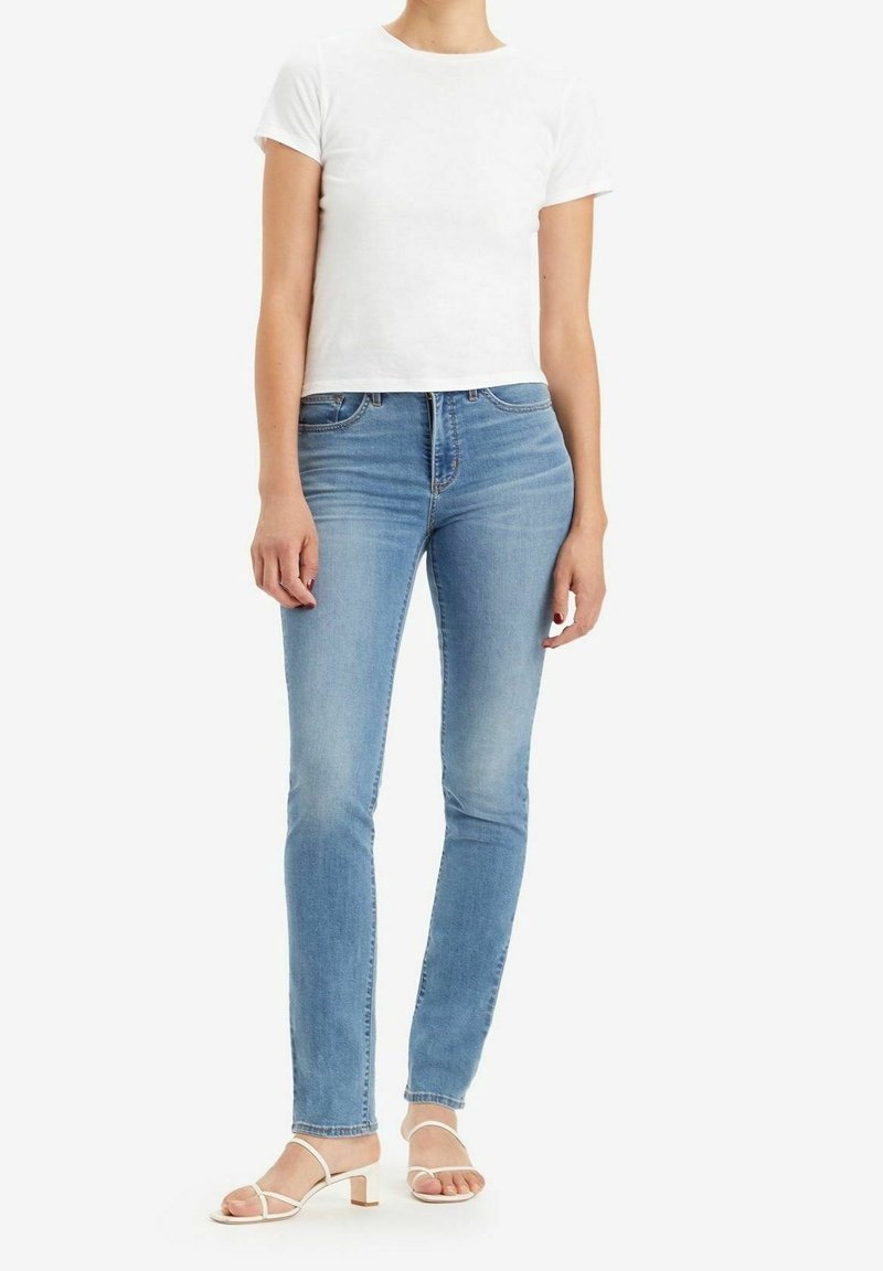 Ljusblå smala jeans i denim, kombinerade med en åtsittande vit t-shirt i bomull och vita sandaler med remmar.