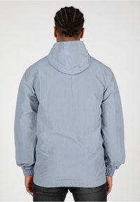 Helle blaue Kapuzenjacke aus strukturiertem Stoff. Verfügt über elastische Bündchen und eine lockere Passform mit einem einfachen, schlichten Design.