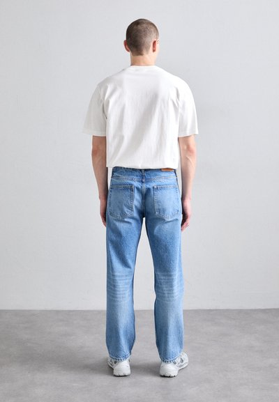 Camiseta blanca de manga corta combinada con vaqueros rectos de color azul claro. Los vaqueros tienen un aspecto desgastado con decoloración y cinco bolsillos.