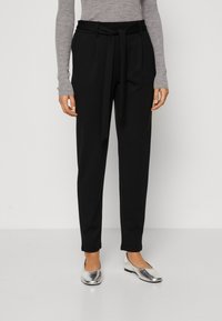 Black tailored trousers with a waist tie, featuring a straight leg design. Worn with silver flats and a light grey long-sleeve top.