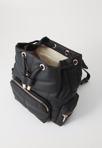 Sac seau en tissu matelassé noir avec quincaillerie dorée, fermeture à cordon, et poche zippée à l'avant. L'intérieur présente une doublure de couleur claire.