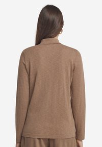 Brun långärmad topp med krage, mjukt material och avspänd silhuett. Har en rak fåll och något avsmalnande ärmar.