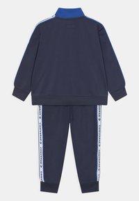 Conjunto de chándal azul marino con un cuello alto, acentos en azul contrastante en las mangas y bandas laterales que presentan texto de marca en blanco en los pantalones.