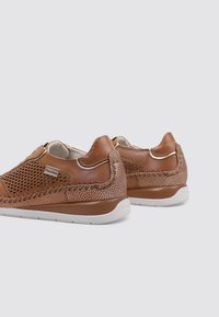 Zapatos de cuero marrón con diseño perforado, detalles trenzados, suelas acolchadas y suela exterior de goma blanca contrastante.