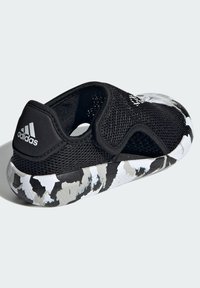 Scarpa nera in rete con retro testurizzato, dotata di cinturino regolabile e un design unico della suola in camouflage bianco e nero.