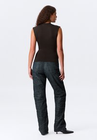 Tettsydd, mørkebrun ermeløs topp kombinert med løse, teksturerte mørkeblå jeans med bølgete mønster. Stylet med svarte hælsko.